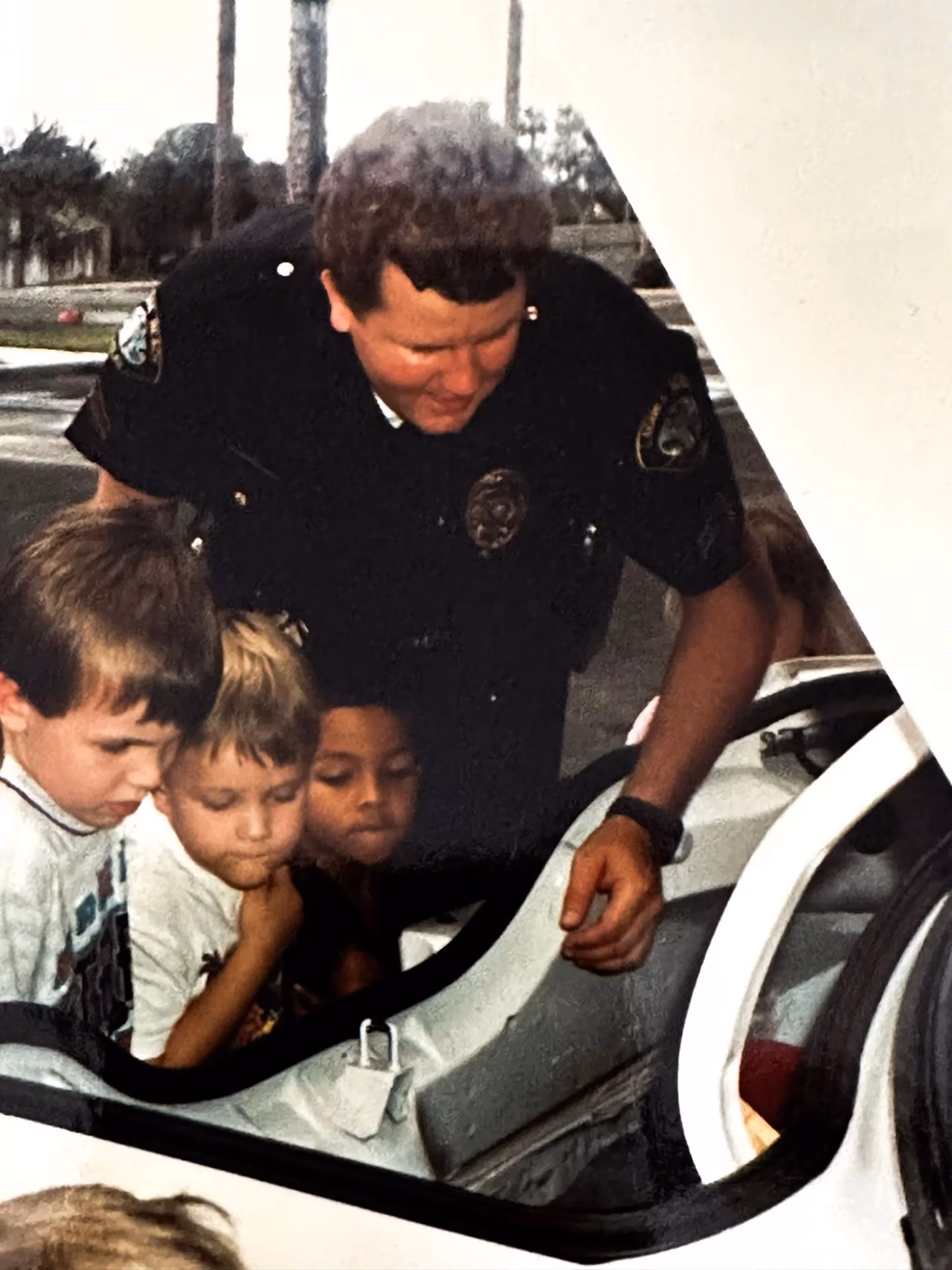 Archival photograph of a young Officer Fehlman showing neighborhood children the inside of his patrol car